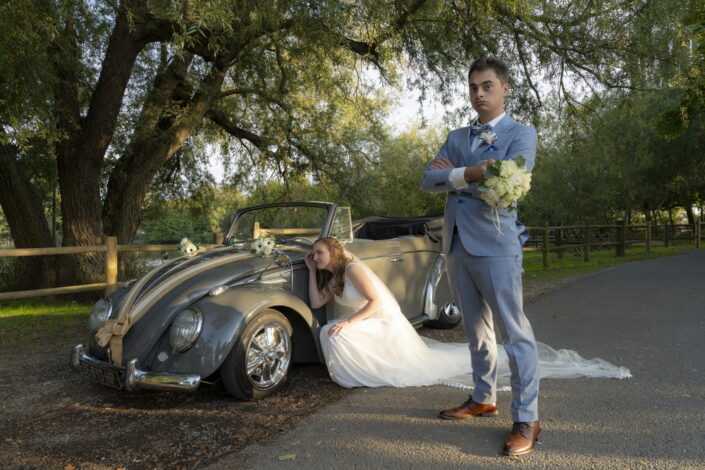 La mariée se recoiffe en se regardant dans le rétroviseur de la voiture pendant que le marié attend
